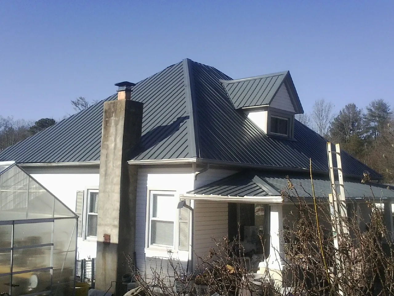 Dark blue standing seam metal roof on a white farmhouse with dormer — Slate & Tile Roof Repair by Roofing Brothers in Fort Blackmore