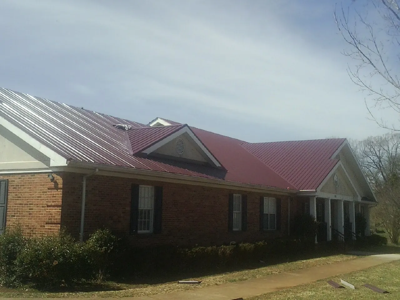 Red metal roof with gabled entries on a long brick building, from a Hail Damage Roof Repair job in Fort Blackmore