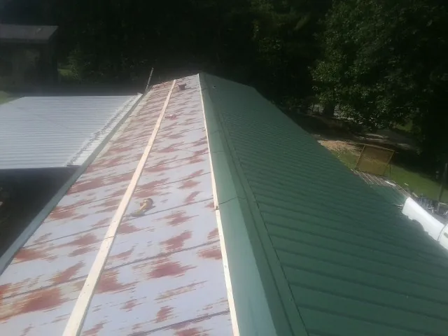Old rusted panels beside newly installed green metal roofing — Wind Damage Roof Repair by Roofing Brothers in Fort Blackmore