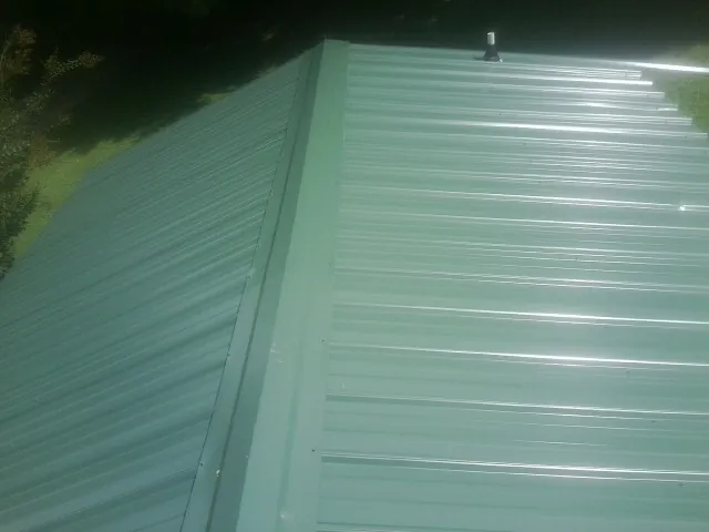 New green metal panels meeting at the ridge of a roof — Flat Roof Repair work by our crew in Fort Blackmore