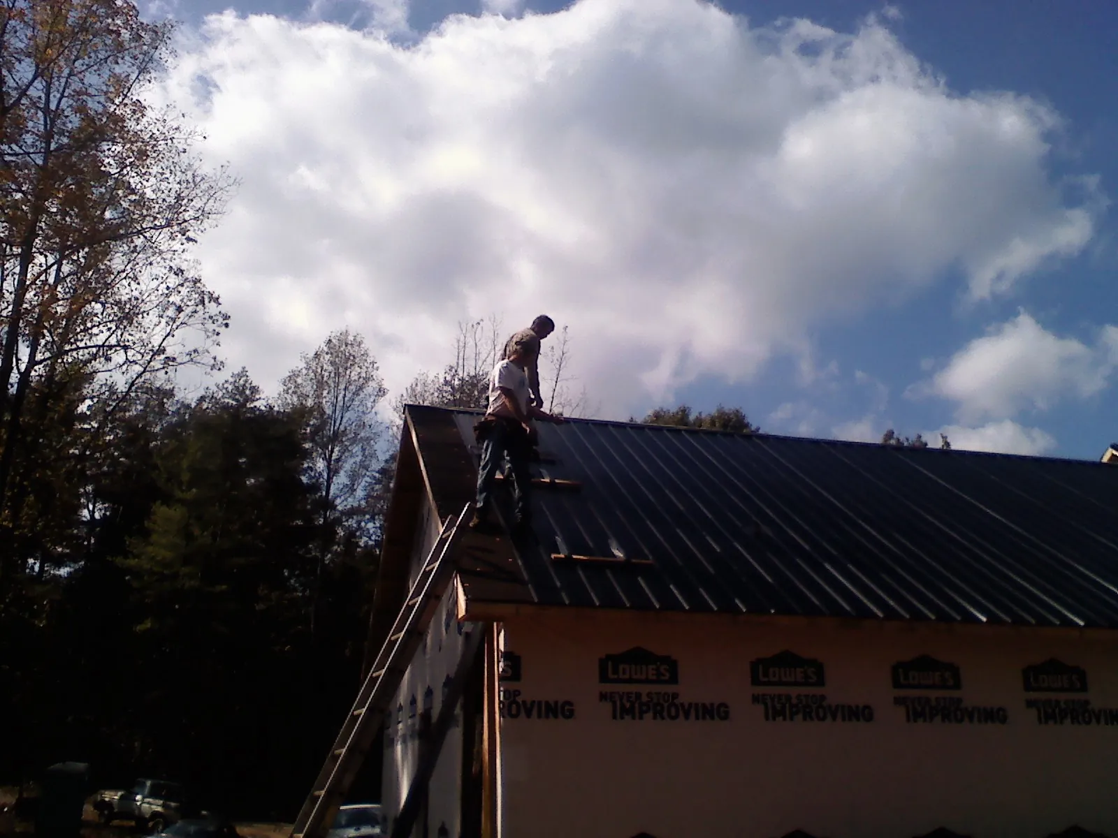 Roofer fastening dark metal panels high against a cloudy sky, from a Roof Inspection job in Fort Blackmore