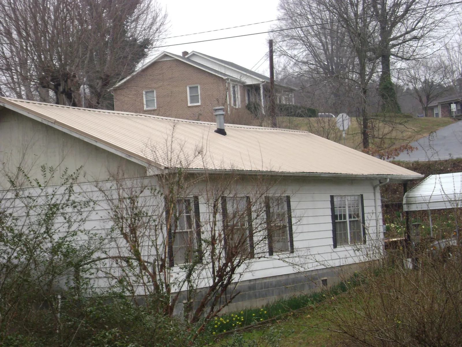 Tan metal roof on a white sided house set into a hillside — Commercial Roofing by Roofing Brothers in Fort Blackmore