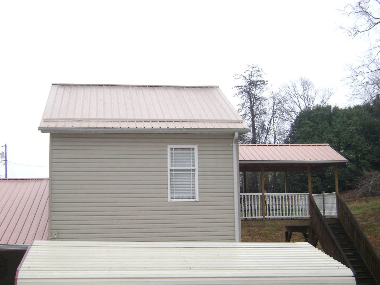 Tan metal roofs on a two story addition and attached porch, from a Roof Replacement job in Fort Blackmore